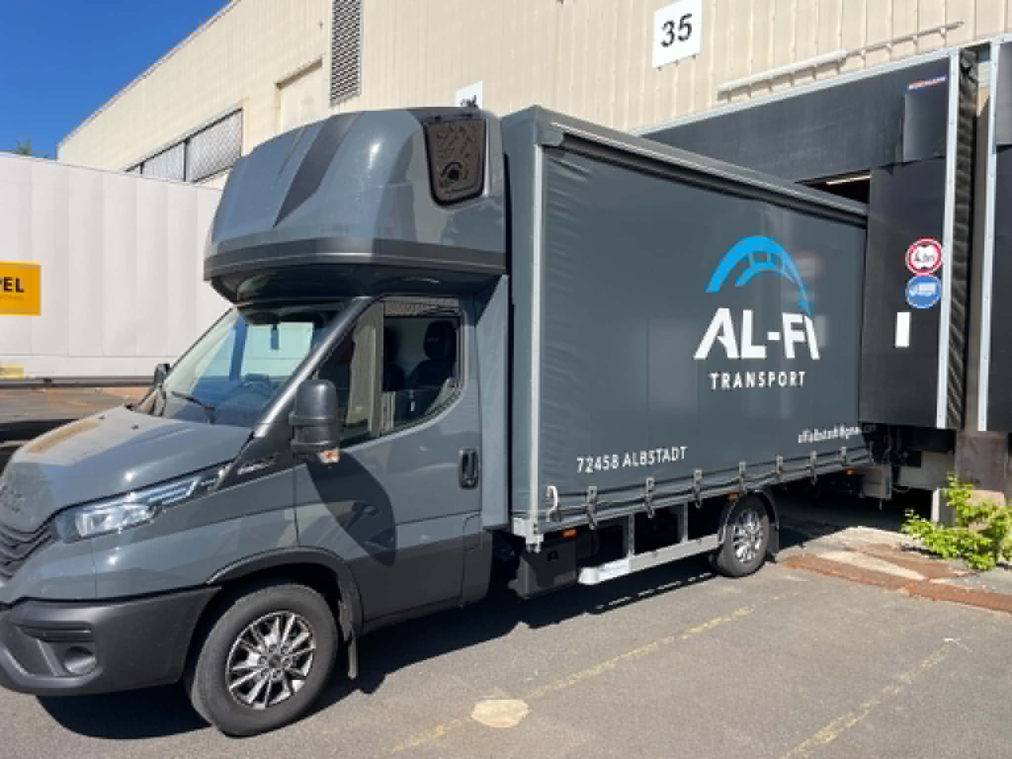 Grauer AL-FI Transporter mit Schiebeplane an einer Laderampe